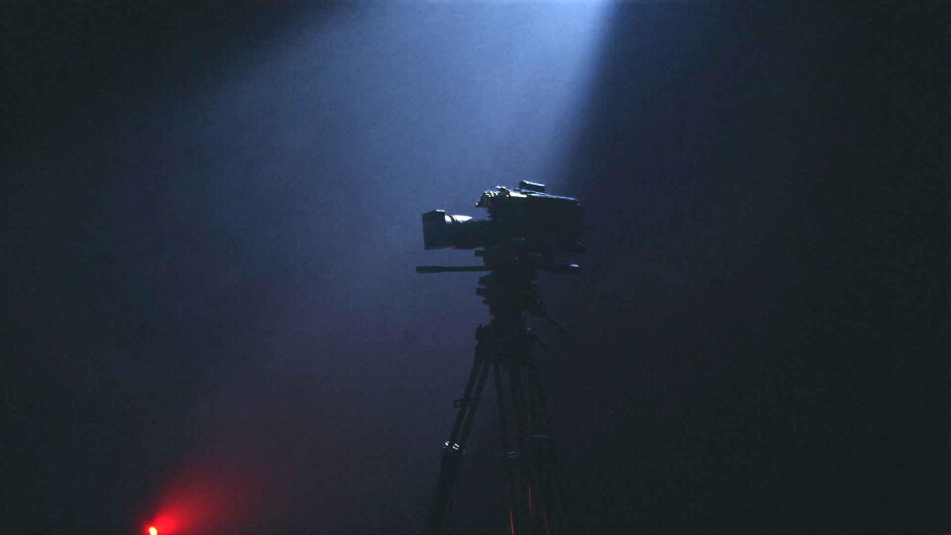A cinema camera on a tripod in a beam of studio light.